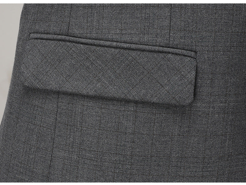 Close-up of gray suit jacket pocket showing tailored flap detail and fine wool texture against neutral background.