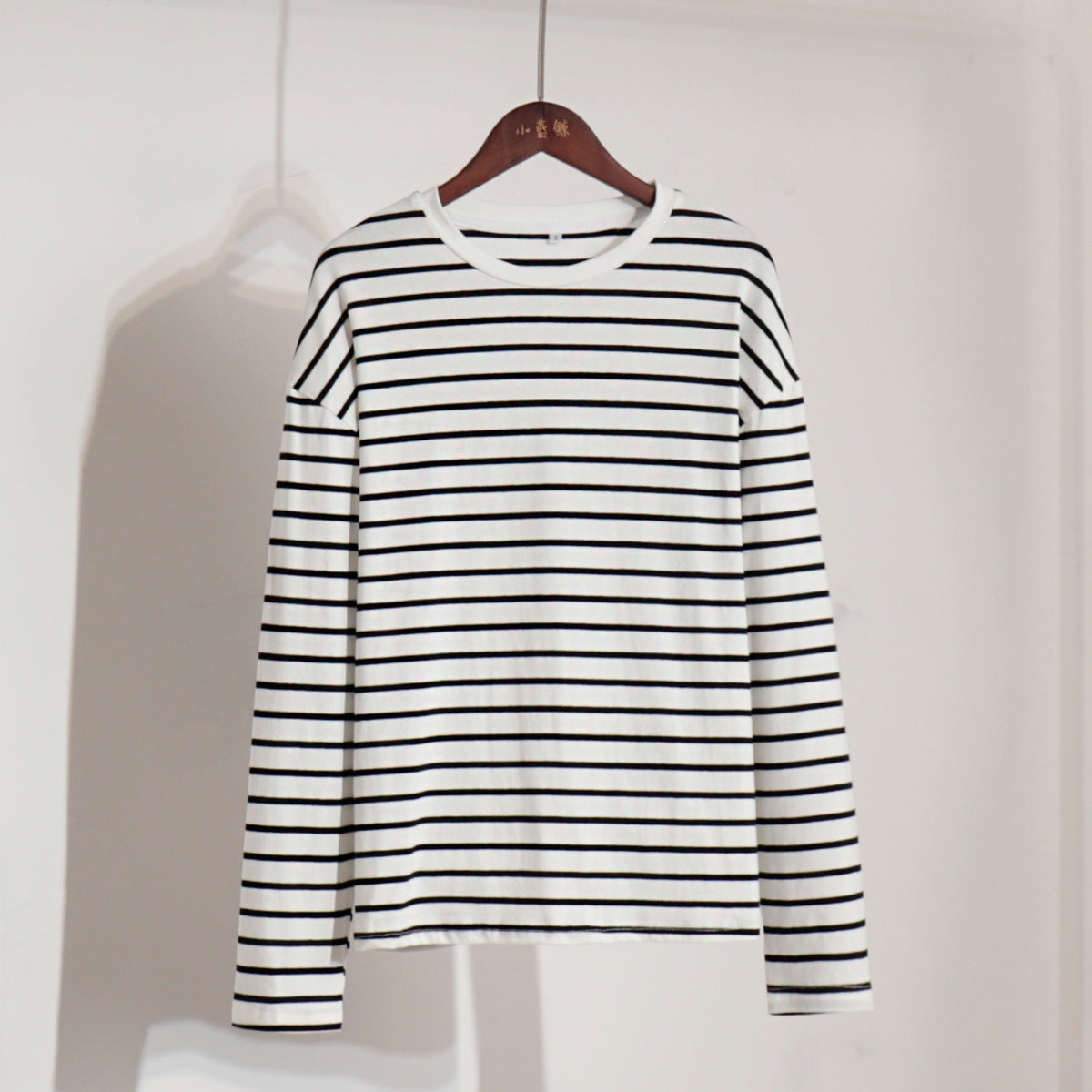 White and navy striped long-sleeve shirt on wooden hanger against white background