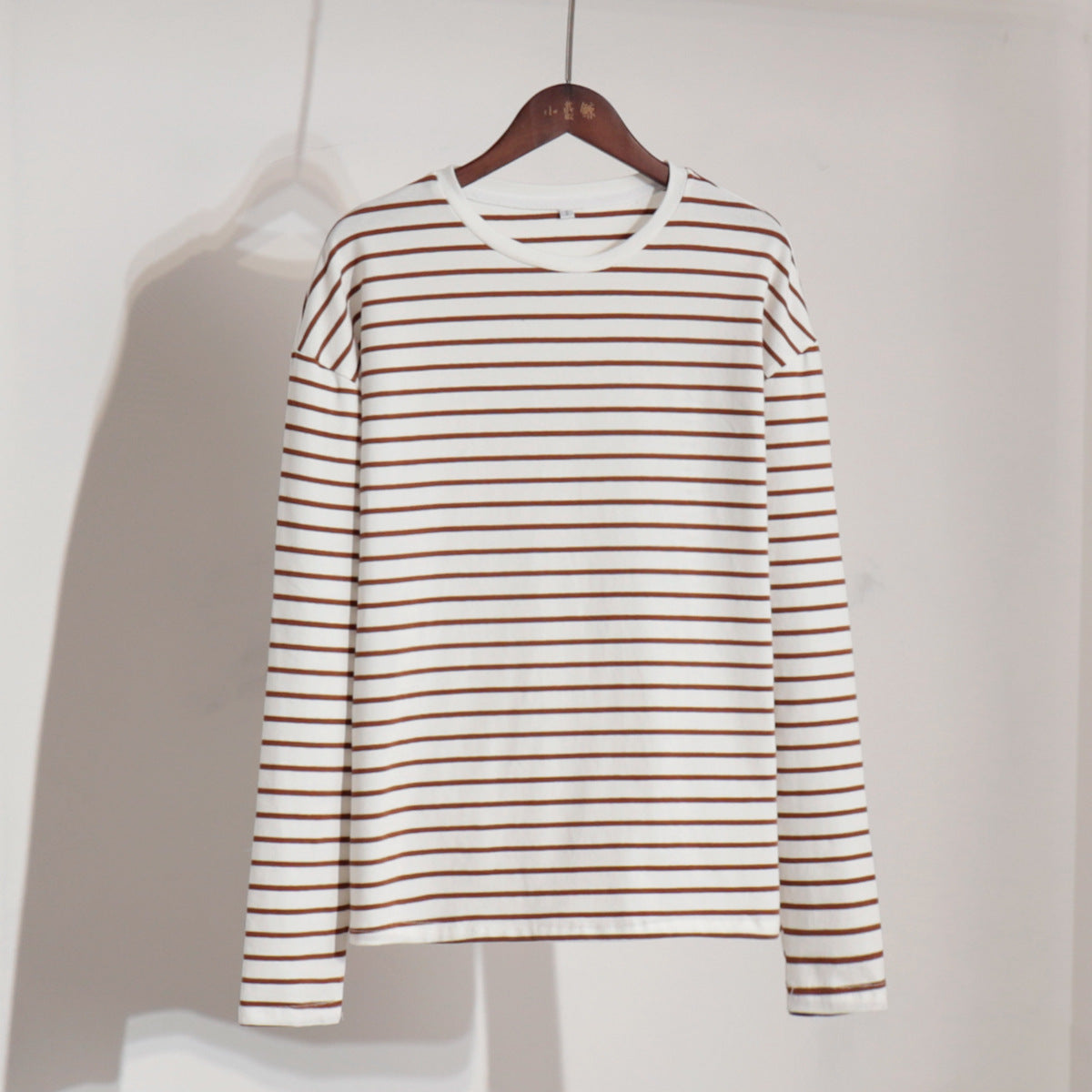 White and brown striped long-sleeve shirt on wooden hanger against white backdrop