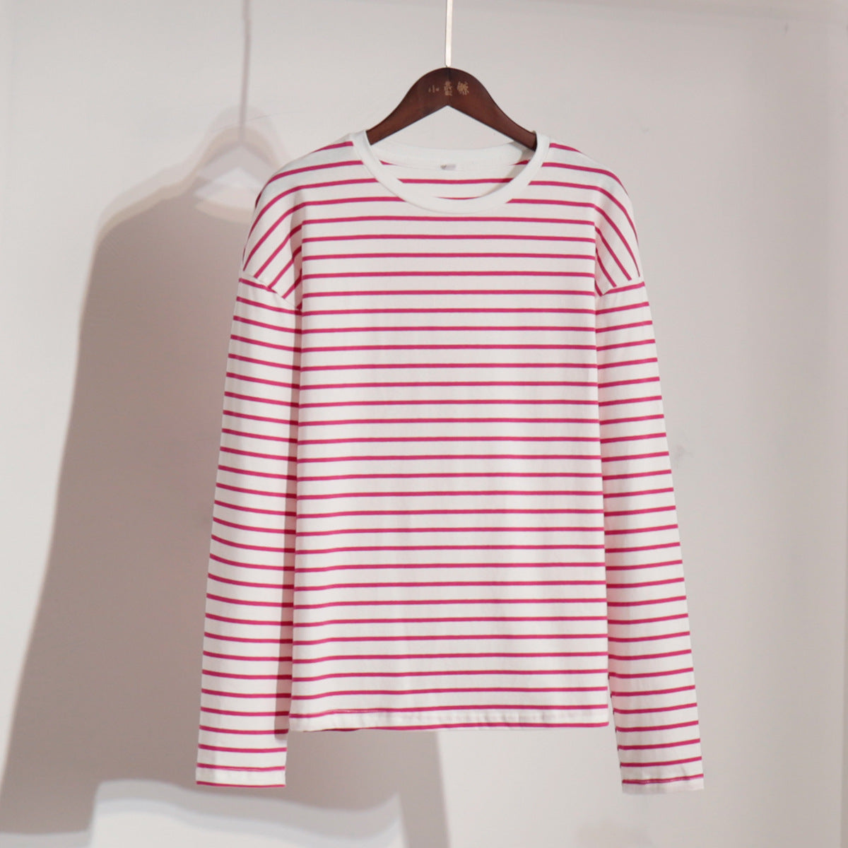 White and red striped long-sleeve shirt on wooden hanger against white wall