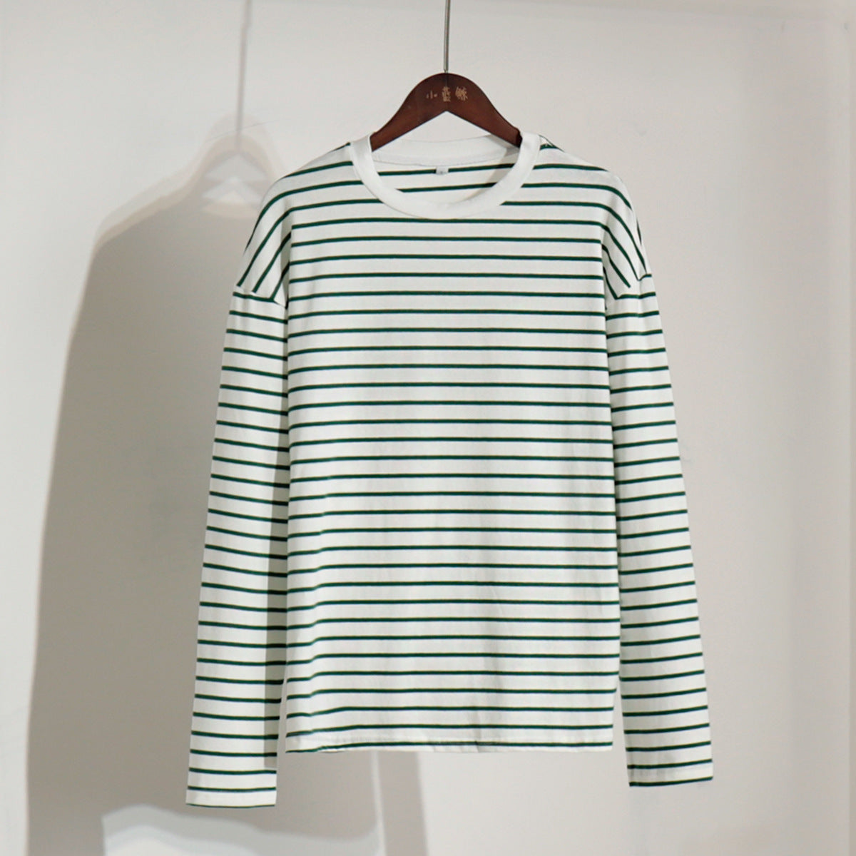 White and green striped long-sleeve shirt hanging on wooden hanger
