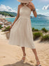Pleated cream midi dress with halter neckline and fitted waist, styled with white sandals and beach backdrop