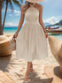 Woman in cream pleated halter dress on beach, accessorized with straw hat and beaded bracelets