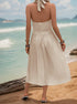 Back view of cream pleated halter dress showing tied neck detail and midi length, beach setting