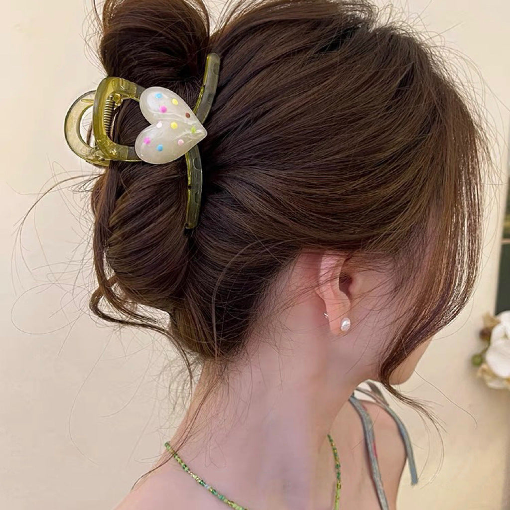 A close-up of a translucent green heart-shaped hair claw with pastel polka dots on a clear clip.