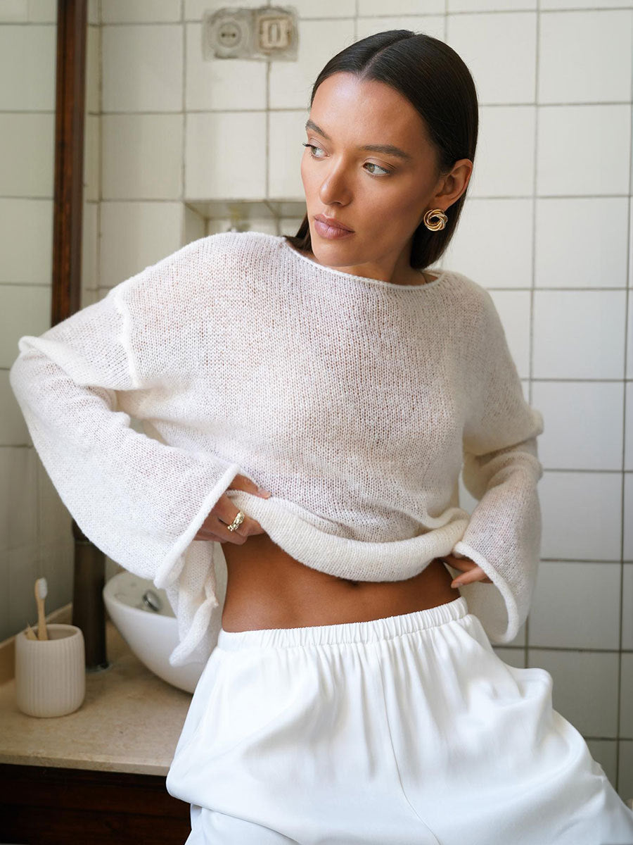 White knit sweater with wide boat neck and bell sleeves, paired with white elastic waist pants, worn with gold spiral earrings