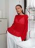 Red oversized knit sweater with geometric pattern detail, styled with white pants in modern kitchen setting