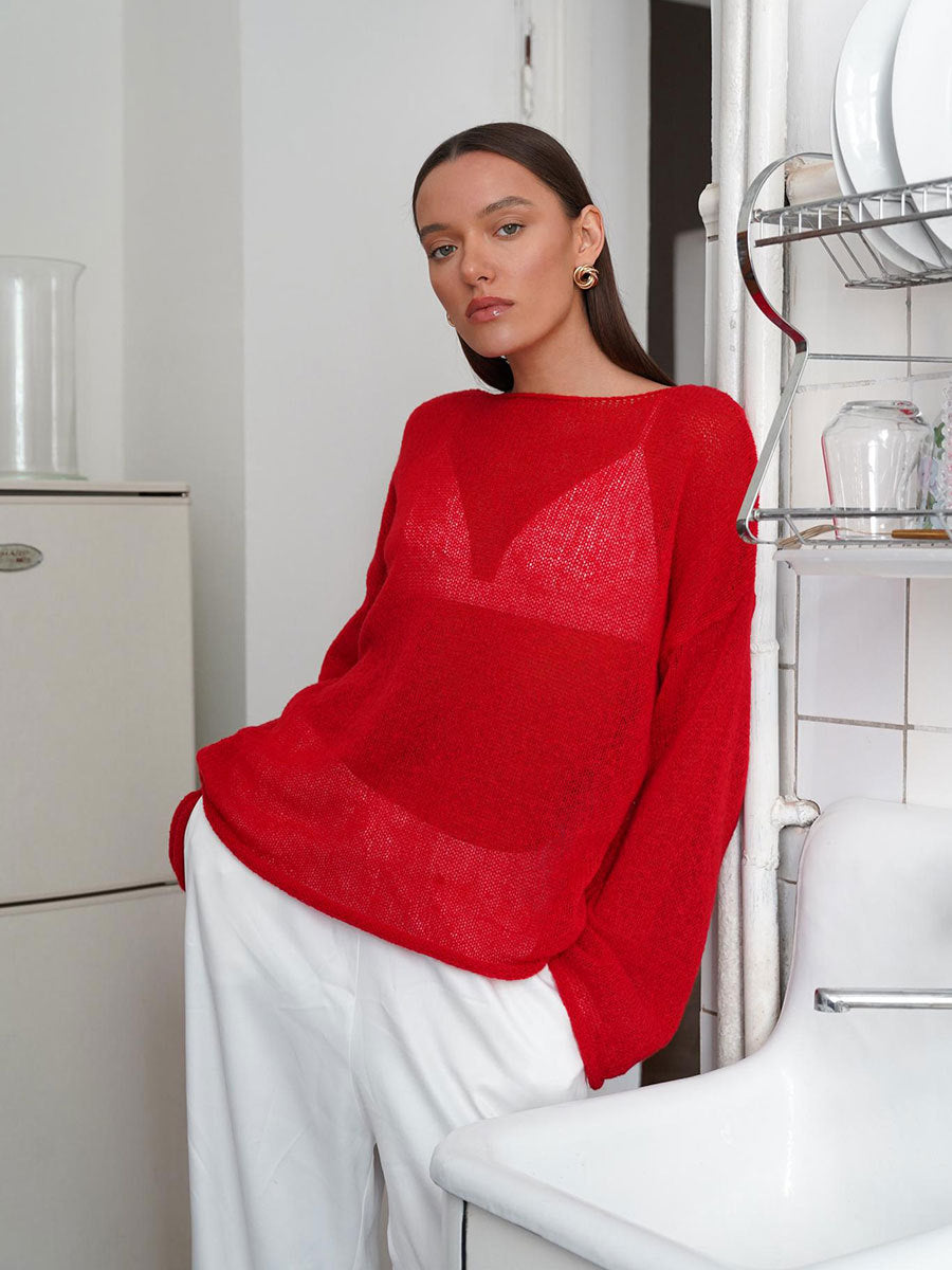 Red oversized knit sweater with geometric pattern detail, styled with white pants in modern kitchen setting