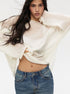 White loose-knit sweater with casual twist detail, paired with distressed blue jeans, model with long flowing dark hair