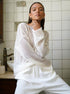 Oversized white knit sweater with relaxed neckline and loose sleeves, styled with white wide-leg pants and gold statement earrings