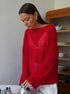 Red knit sweater with boat neckline and relaxed fit, styled with white pants, photographed in kitchen setting