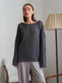 Gray knit sweater with boat neckline and classic silhouette, paired with light gray pants, table lamp in background