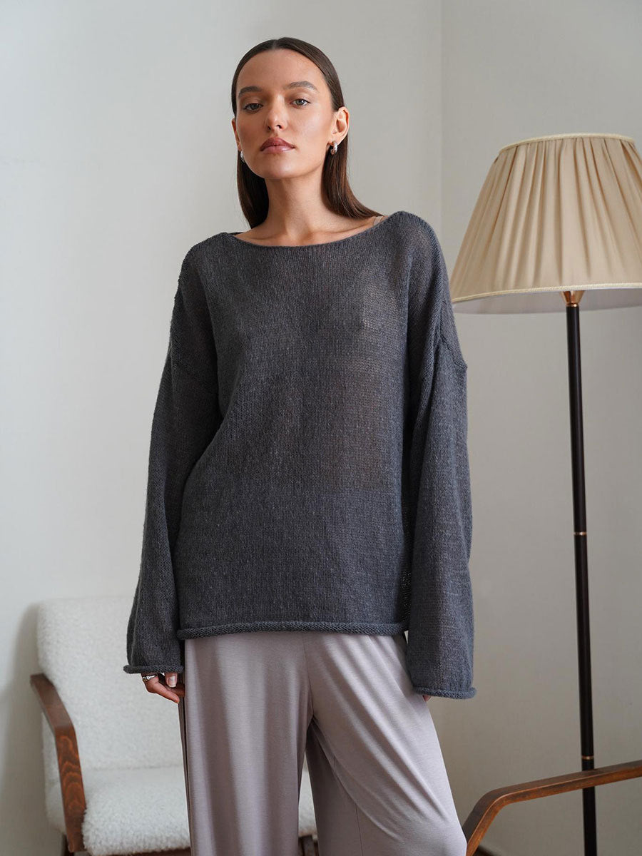 Gray knit sweater with boat neckline and classic silhouette, paired with light gray pants, table lamp in background