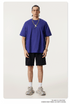 Model in royal blue oversized t-shirt with short sleeves, black shorts, white socks and chunky trainers, accessorized with silver chain necklace
