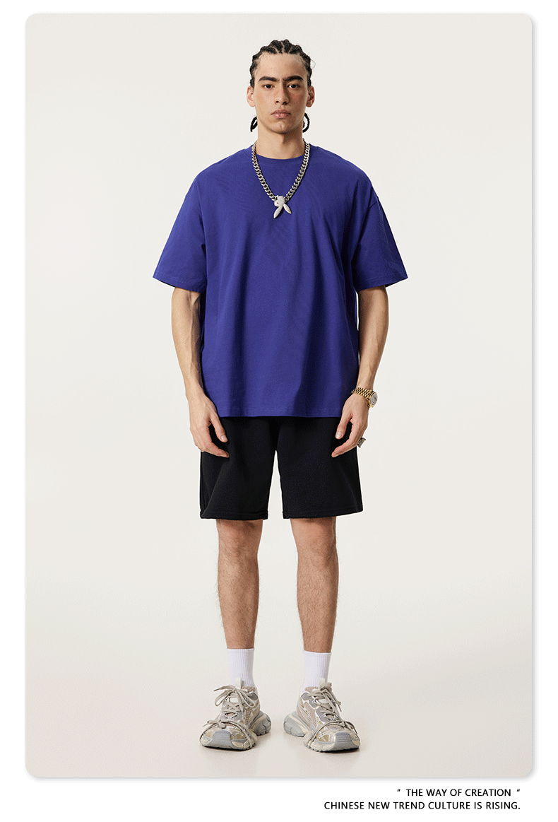 Model in royal blue oversized t-shirt with short sleeves, black shorts, white socks and chunky trainers, accessorized with silver chain necklace