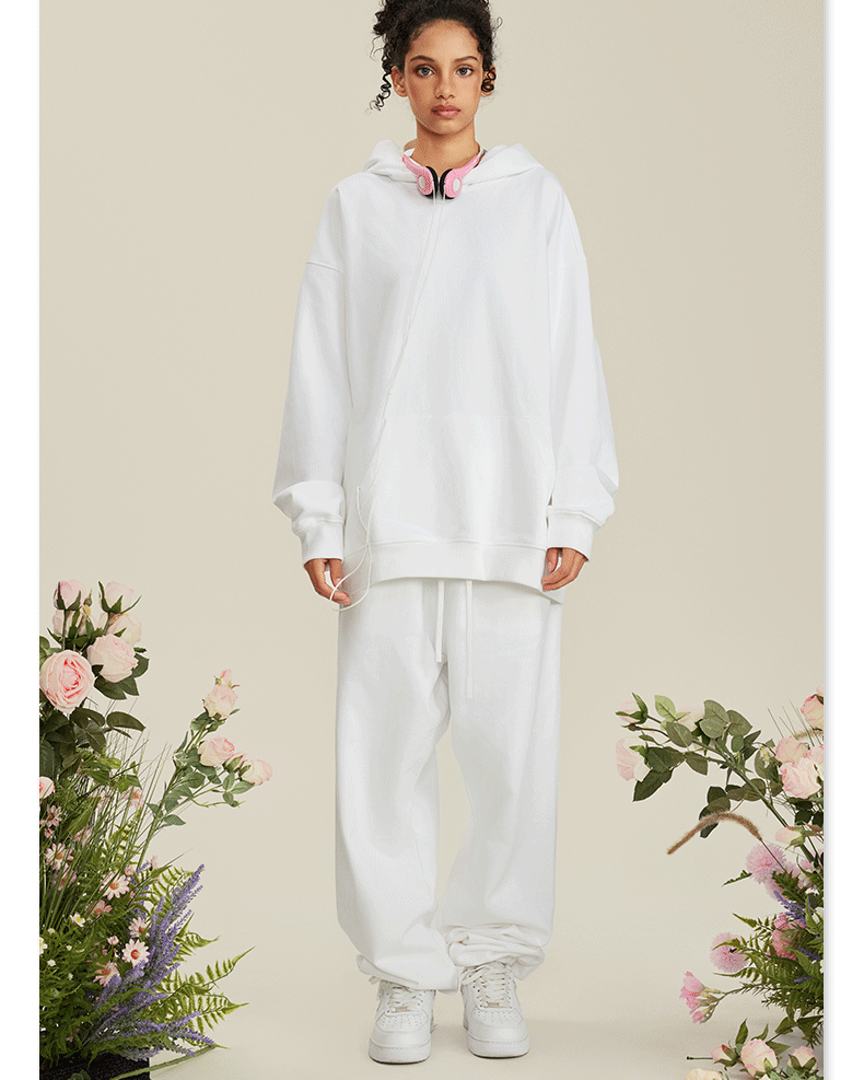 Woman wearing all-white hoodie and sweatpants set with pink headphones around neck among roses