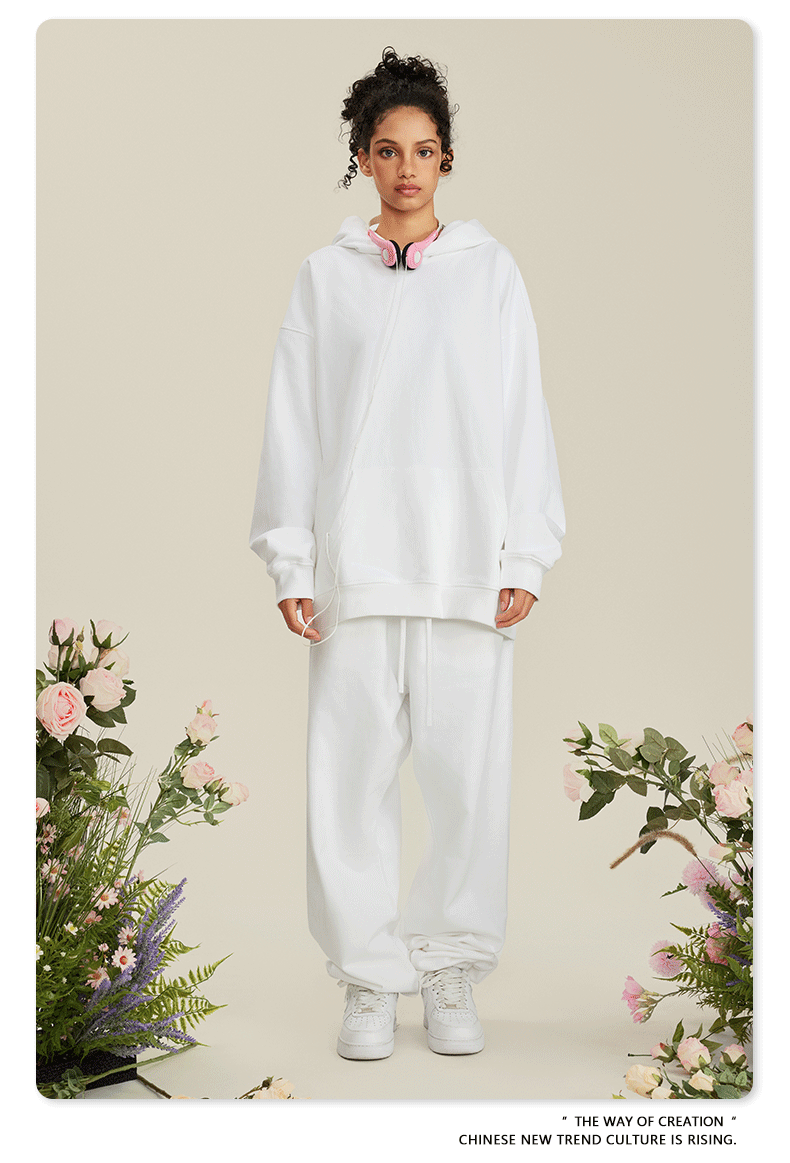 Woman wearing all-white hoodie and sweatpants set with pink headphones around neck among roses