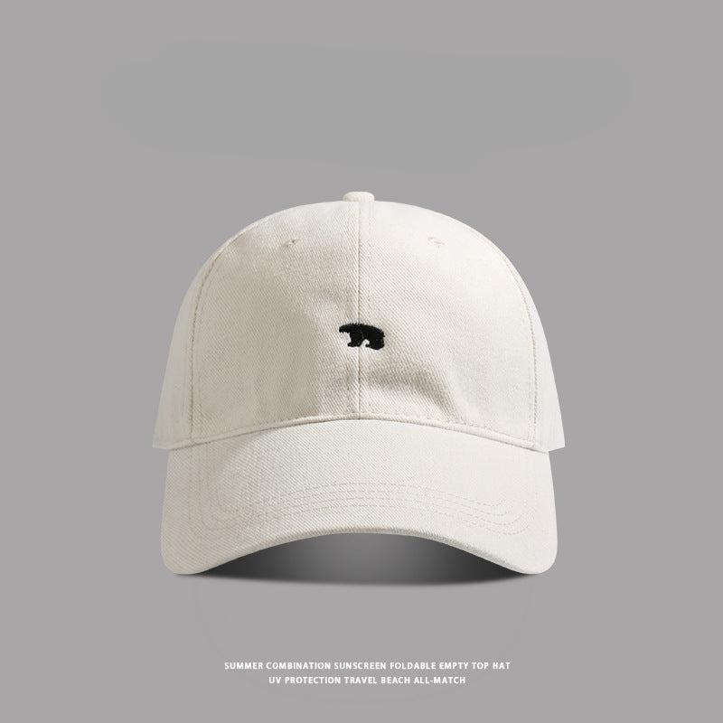 White baseball cap with small black bear embroidery - A minimalist white dad hat featuring a tiny black bear logo stitched on the front