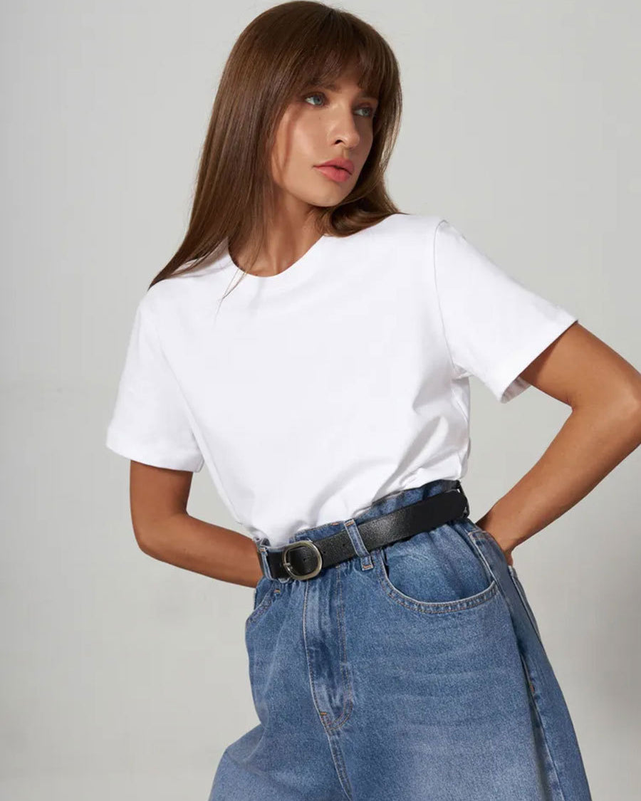White T-Shirt Outfit – Model wears a white crew-neck T-shirt tucked into high-waisted blue jeans with a black belt