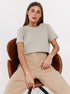 Light Beige T-Shirt Outfit – Model sits on a brown chair wearing a light beige T-shirt and high-waisted beige pants