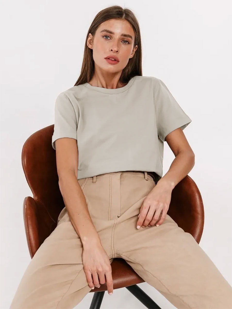 Light Beige T-Shirt Outfit – Model sits on a brown chair wearing a light beige T-shirt and high-waisted beige pants