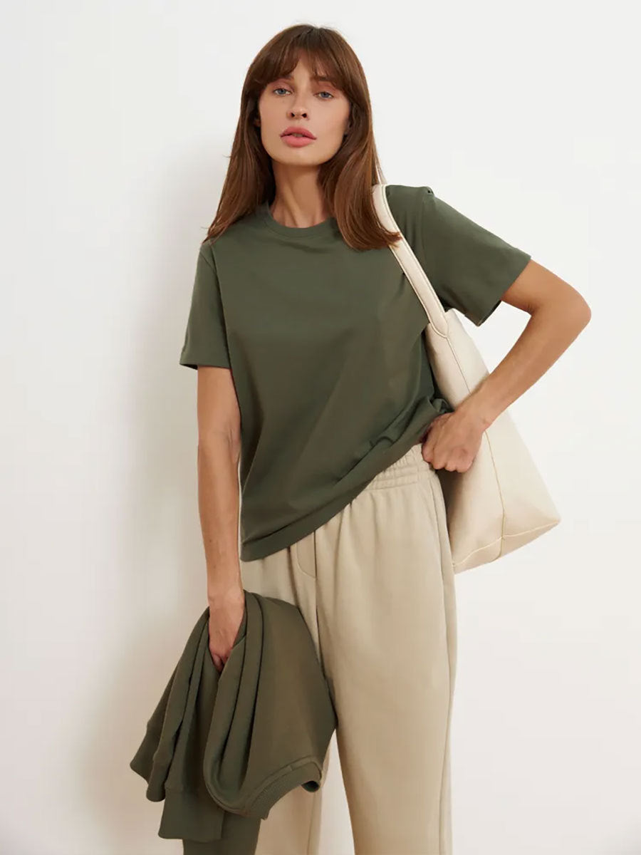 Olive Green T-Shirt Outfit – Model in an olive green T-shirt and beige sweatpants, carrying a cream tote and matching sweatshirt