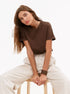 Brown T-Shirt Outfit – Model sits on a stool in a brown crew-neck T-shirt and wide-leg beige pants