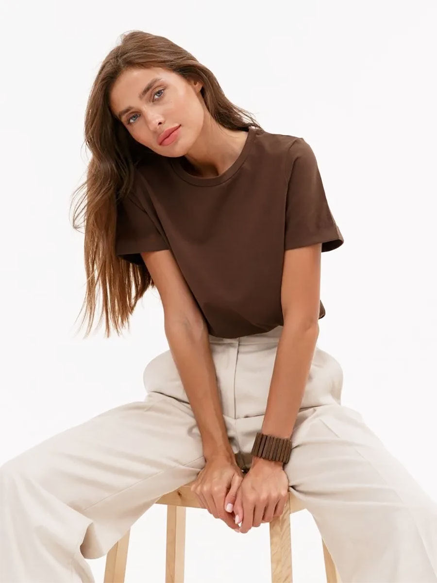 Brown T-Shirt Outfit – Model sits on a stool in a brown crew-neck T-shirt and wide-leg beige pants