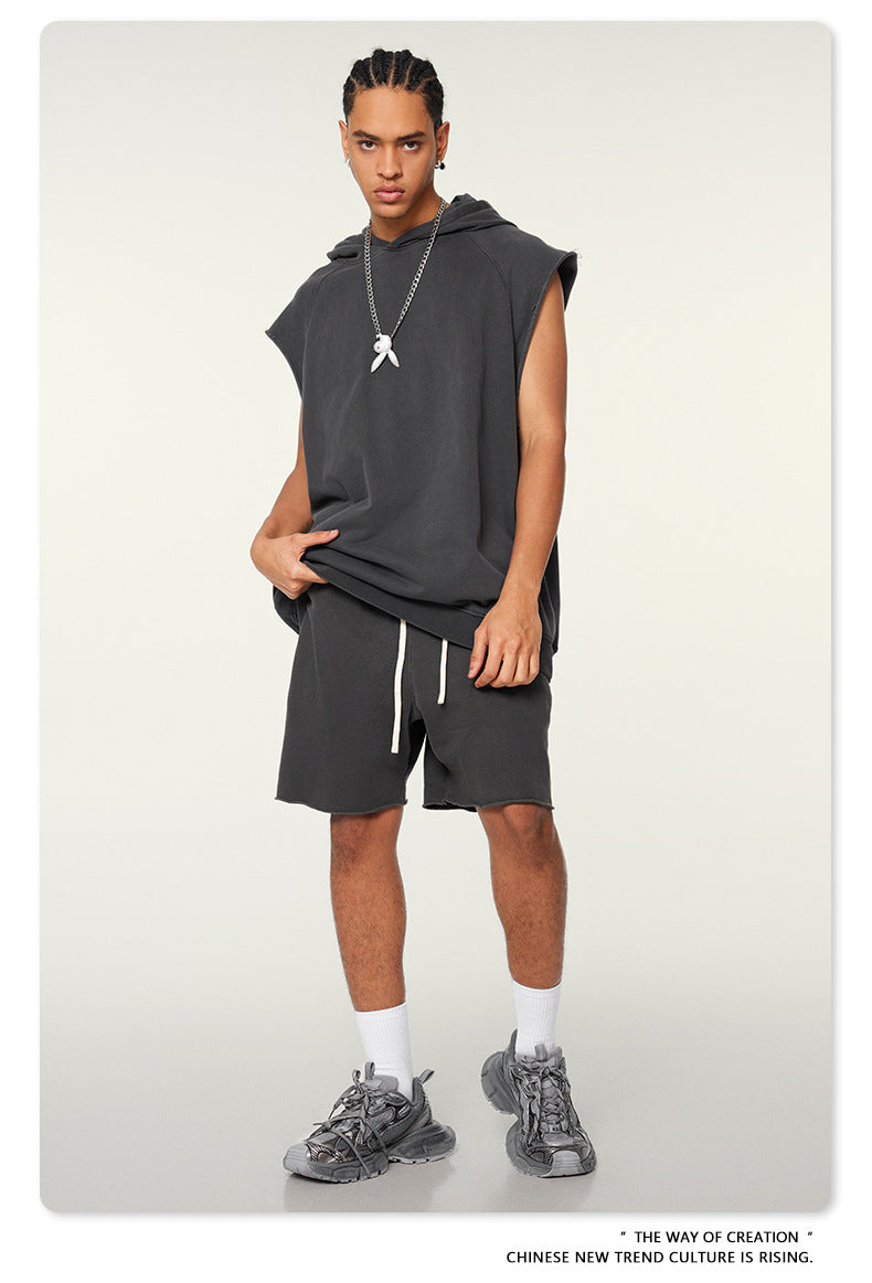 A model wearing charcoal sleeveless hoodie with matching shorts, silver pendant necklace and gray athletic shoes against white background