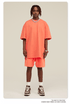 Man with dreadlocks wearing coral/peach oversized T-shirt and shorts set with white sneakers and silver jewelry