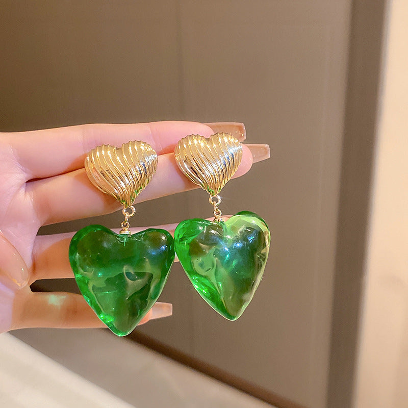 Gold heart-shaped drop earrings with translucent green gemstone pendants held in hand showing statement jewelry proportion