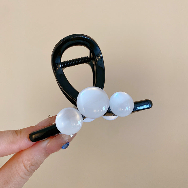 A black resin hair claw with glossy white beads, held between fingers with glossy nail art.
