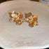 Gold Floral Stud Earrings – Textured gold flower-shaped stud earrings with a hammered finish, placed on a ceramic plate