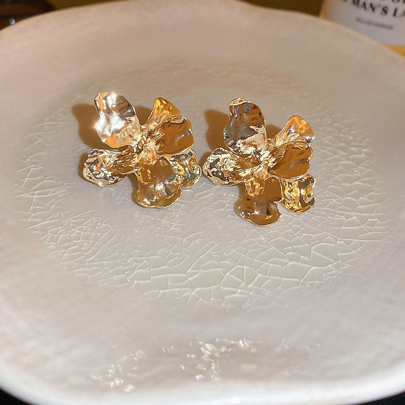 Gold Floral Stud Earrings – Textured gold flower-shaped stud earrings with a hammered finish, placed on a ceramic plate