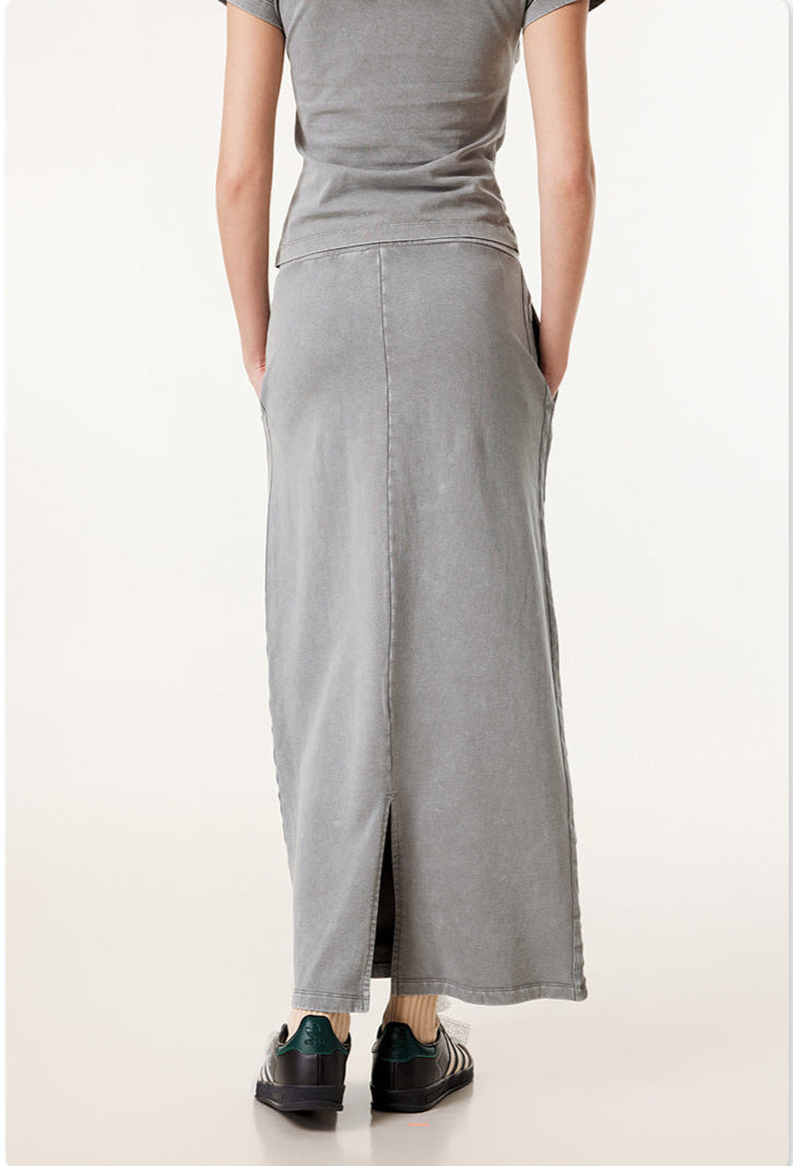 Rear view detail of long gray denim skirt showing center back seam and waistline, with black sneakers