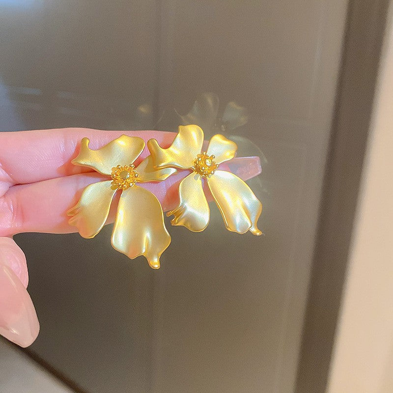Satin Gold Flower Earrings – Large gold flower earrings with satin petals and a beaded center, held against a neutral background