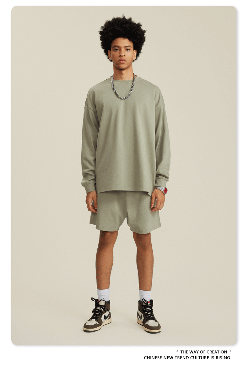 Man in sage green sweatshirt and shorts set with chain necklace, watch and white sneakers