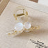 A clear acrylic hair claw with two glossy white resin beads, set on a beige fabric surface.