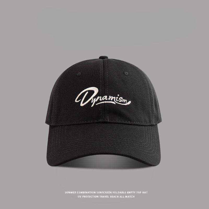 Black baseball cap with white Dynamism script embroidery against gray background"