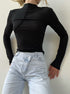 Minimalist black mock neck top with asymmetrical seam detail, tucked into light wash asymmetric button jeans