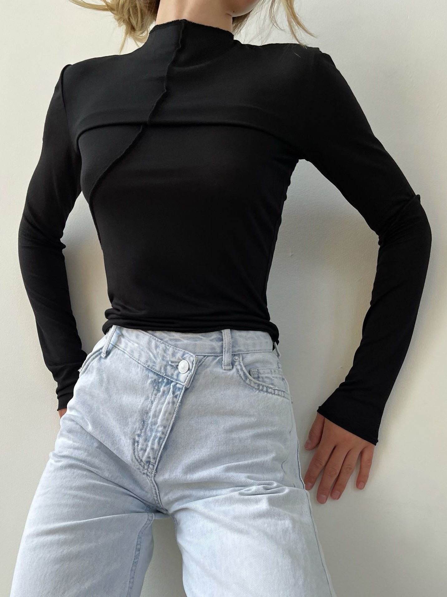 Minimalist black mock neck top with asymmetrical seam detail, tucked into light wash asymmetric button jeans