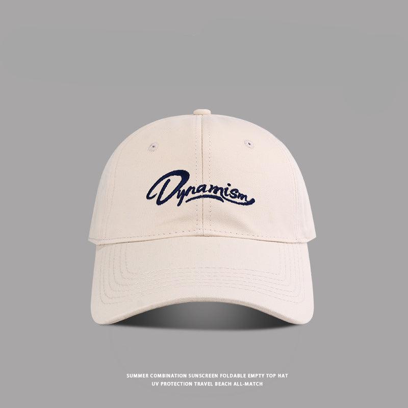Beige colored baseball cap featuring navy Dynamism script logo