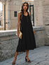 Black midi dress with side slit, model holding nude clutch, wearing black strappy heels in stone-walled setting