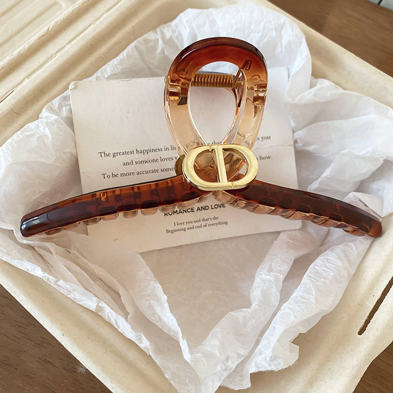 A large amber-colored resin hair claw with a gold buckle, placed on a soft beige surface with elegant paper text.