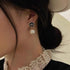 Black and white floral drop earring with crystal rim and pearl pendant, shown worn on ear with lace collar