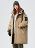 A woman with curly red hair wearing olive beanie and beige/olive technical parka with large pockets poses against white background