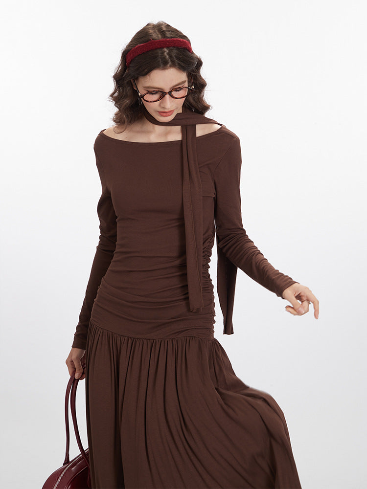 Close-up front view of brown maxi dress showcasing ruched side panels, asymmetrical neckline construction, and draped fabric detail