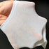 Close-up of white mesh ankle sock being held in hand showing lightweight breathable fabric construction and ribbed edge against dark background