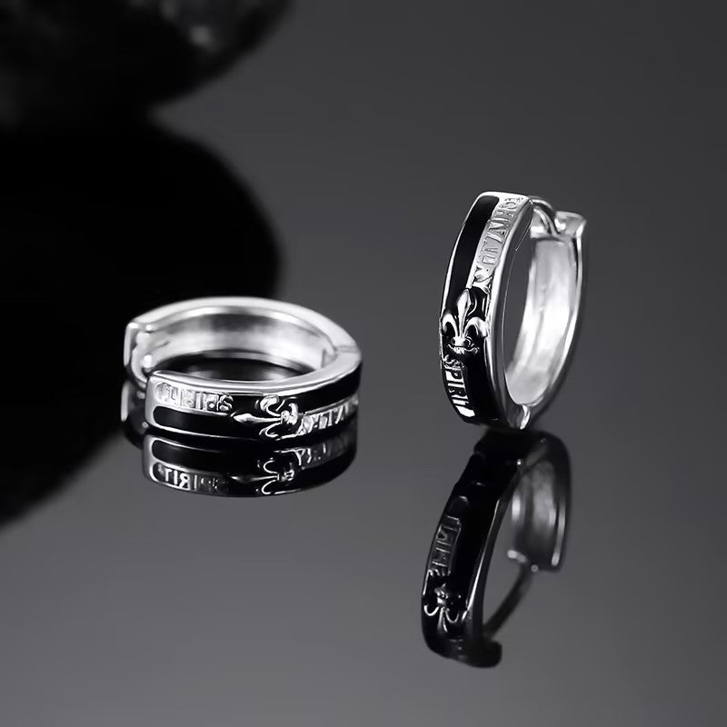 Stainless steel huggie hoops with black enamel band and fleur-de-lis pattern on reflective surface