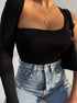 Close-up of a woman in a black asymmetrical bodysuit with long sleeve, accessorized with gold necklaces and a black woven bag.